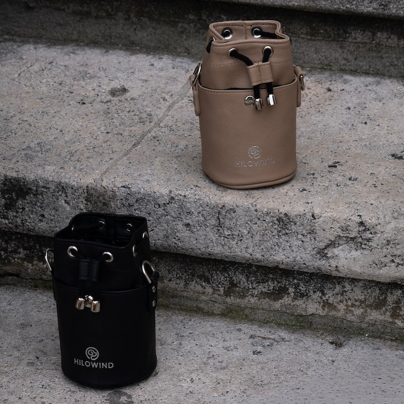 Zwei Leckerlibeutel in schwarz und beige von HILOWIND, stehend auf einer Treppe.