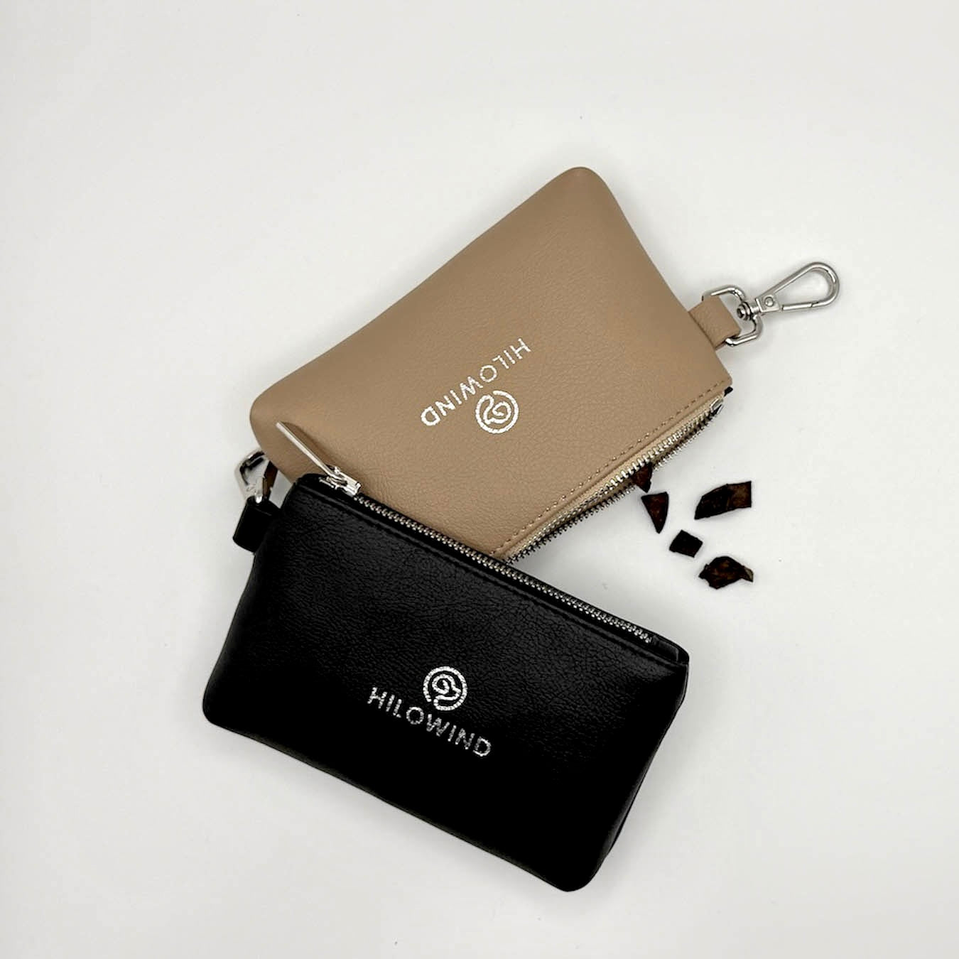 Leckerlitaschen von HILOWIND aus veganem Apfelleder in den Farben beige und schwarz. Flatlay Aufnahme mit Leckerlis, die aus der Tasche fallen.